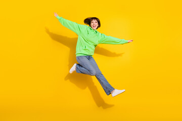 Full size photo of cheerful young happy cute woman jump up good doom hands wings isolated on yellow color background