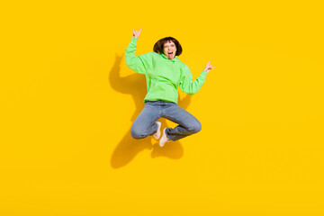 Full length body size view of lovely crazy cheerful girl jumping showing horn grimacing isolated over bright yellow color background