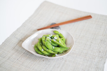 Green pea pods on white plate with wooden chopsticks on mat in Japanese restaurant, close-up