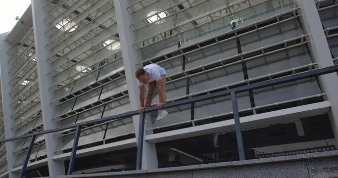 Professional acrobat performing dangerous trick on the railings against backdrop of modern stadium. Caucasian guy  making a handstand with straddle split on a narrow metal pipe
50 fps slow motion
