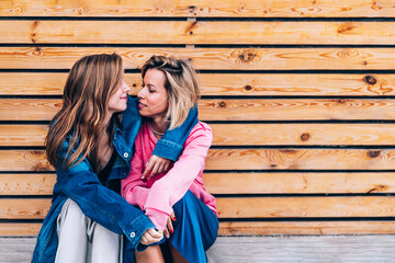 Teenage daughter with mother sitting in front of wooden wall