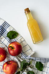 Apfelsaft in einer Glasflasche und rote Äpfel auf einem karierten Geschirrtuch. Weißer...