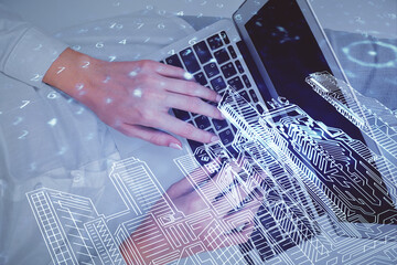 Double exposure of woman hands working on computer and buildings construction hologram drawing. Top View. smart city concept.
