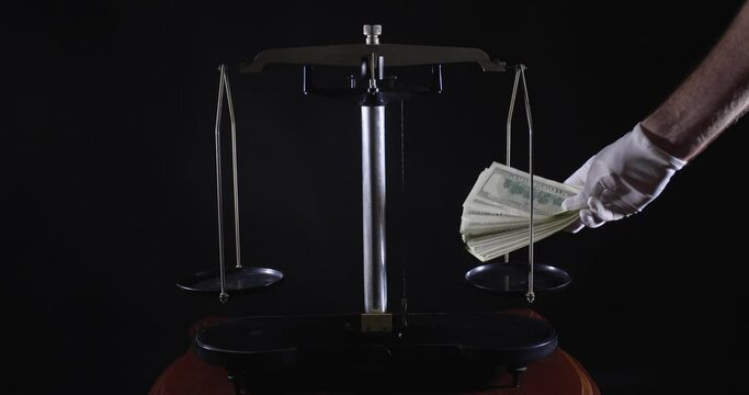Unrecognizable people in white gloves put bundles of bills on the scales. Venal justice and bribery concept