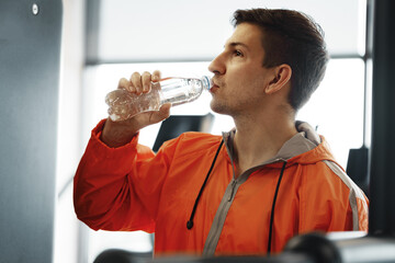 Fototapeta na wymiar Portrait of young man drinking some water from a bottle in a gym