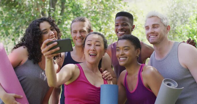 Group of diverse young people holding yoga mats taking a selfie at the park