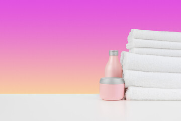Fototapeta na wymiar Pile of towels, bottles with shampoo on white table