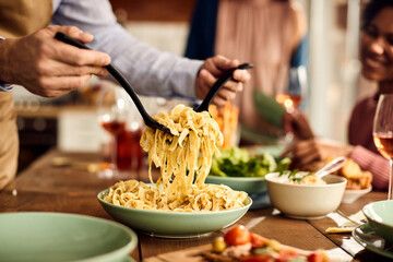 Close-up of man serves pasta at dining table.