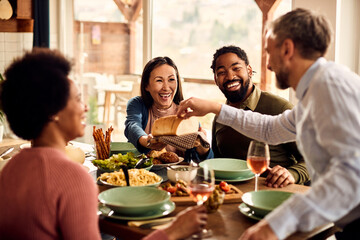 Happy multi-ethnic friends have fun while eating together at dining table.