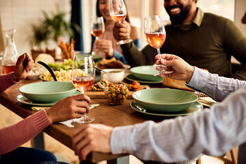 Close-up of multi-ethnic people toast with wine while eating at dining table.
