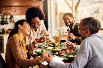 Cheerful friends have fun while drinking wine and having lunch together at home.