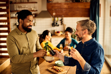 Happy men toast with beer during dinner party in dining room.