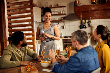 Happy black woman holds a toast while having dinner party with her friends at home.