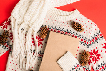 top view of book near pine cones on knitted sweater and red background
