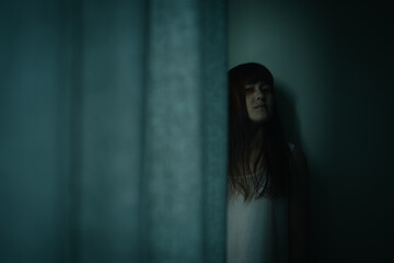 Female ghost in white dress in room. A young scary girl in an old white dress staring in to the camera ferociously with dark background. Asian woman make up ghost face at house. Scary horror concept.