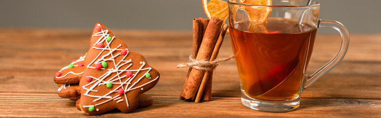 glass cup of tea with sliced orange near cinnamon sticks and gingerbread cookies isolated on grey, banner