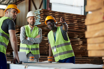 Male workers talks to their manager while having meeting at lumber warehouse.