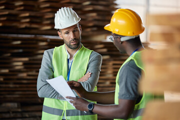 Male inspector and African American worker collaborate while going through checklist at distribution warehouse.