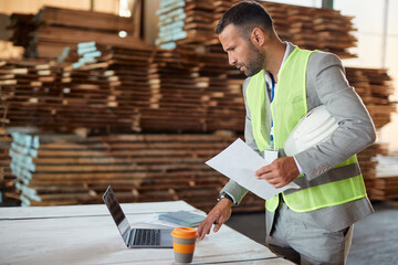 Mid adult manager uses laptop while working at distribution warehouse.