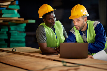 Warehouse manager uses laptop while communicating with worker at storage department.