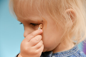 The little girl clumsily paints her makeup and puts shadows on her face.