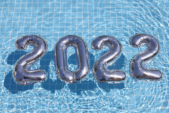 Silver helium balloons with numbers 2022 floating in swimming pool closeup background