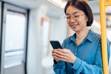 Smiling woman text messaging on smart phone while traveling by public transport.