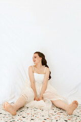 Fototapeta na wymiar Caucasian woman sitting on the floor barefoot dressed in white with tulle skirt and hair braid. Relax, lifestyle and bridal concept