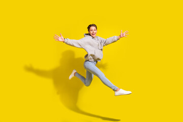 Full length profile photo of funny brown hair young lady jump wear sportcloth jeans sneakers isolated on yellow background
