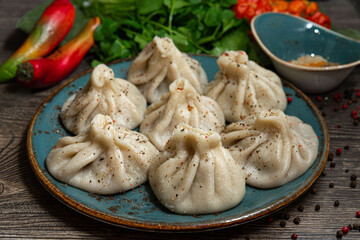 Georgian-style khinkali with meat on a handmade ceramic plate. Sprinkled with ground pepper. Leaves of parsley and coriander in the background. On a dark grey wooden kitchen table.
