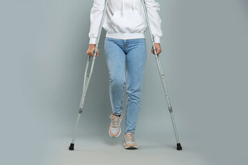 Young woman with axillary crutches on grey background, closeup