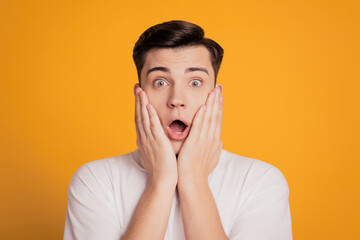 Photo of astonished young man open mouth put hands face isolated on yellow background