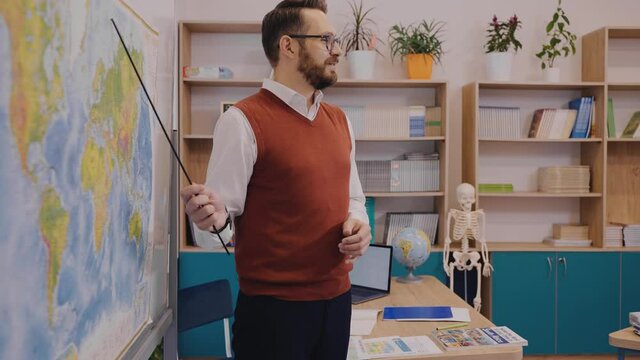Positive male teacher standing at the world map and explaining a topic in geography. Male teacher showing the world map. Modern school with excited and progressive teacher. High quality 4k footage