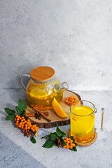 Still life of autumn hot tea from fresh sea buckthorn, mint and orange on a gray stone background. A healthy vegan drink. Medical. Sea buckthorn and mint branch. Health drink ingredients. Autumn. 