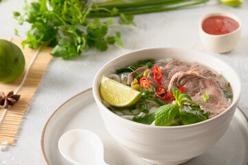 Pho Bo Soup with beef, rice noodles, ginger, lime, chili pepper in bowl on white background. Close up. Vietnamese cuisine.