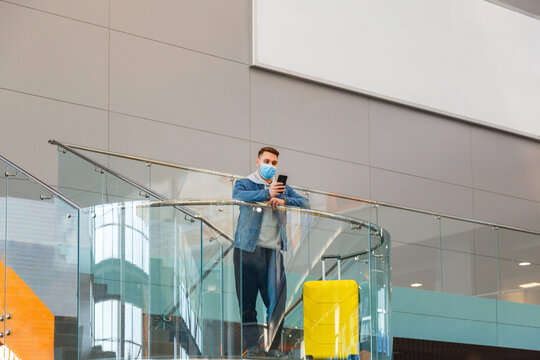 Male traveler Use mobile phone at airport. Man in protective face mask With luggage Use smartphone In airport lounge balcony with outdoor advertising mockup