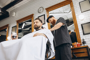 Two handsome men at barbershop. Stylish red-bearded barber and client during haircut process. Beauty, healthcare and male cosmetics concept.