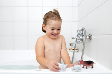 Medium view of adorable chubby wet toddler girl playing in her bath with small tea set and toy...
