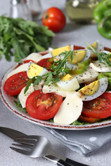 Healthy salad with tomatoes, mozzarella, olives, arugula and eggs on a plate on a light background. Close-up