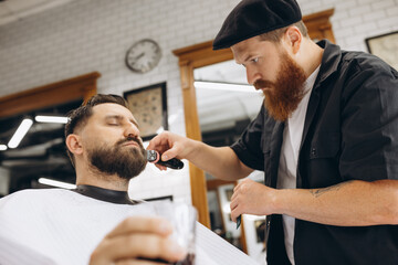 Professional barber, clipper cutting, shaving beard of regular customer at barbershop. Beauty, selfcare, style, fashion and male cosmetics concept.