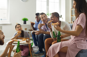 Happy young people eating pizza from carton box at casual gathering at home. Diverse group of friends hanging out, enjoying food, drinking beer, laughing at hilarious joke, having good time together