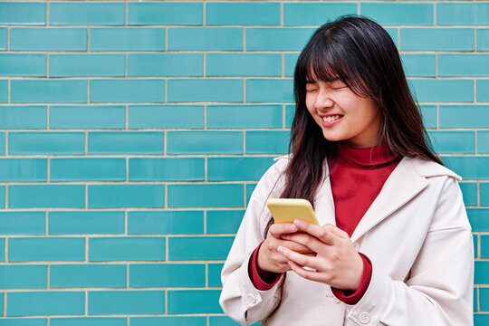 Woman With Eyes Closed Holding Smart Phone In Front Of Turquoise Wall