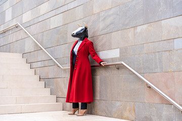 Woman wearing red overcoat and bull mask holding railing while standing near staircase