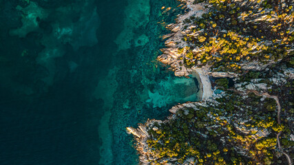 spectacular hidden cove on an island in the mediterranean sea. sunset, golden hour with perfect warm light. Sun makes the soft blue water glow. drone shot,birds eye view, Italy