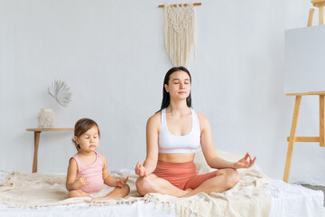 Young mother with her little daughter sitting in lotus position. Meditation and relaxation.