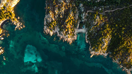 spectacular hidden cove on an island in the mediterranean sea. sunset, golden hour with perfect warm light. Sun makes the soft blue water glow. drone shot,birds eye view, Italy