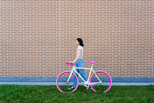 Young woman looking away while wheeling bicycle