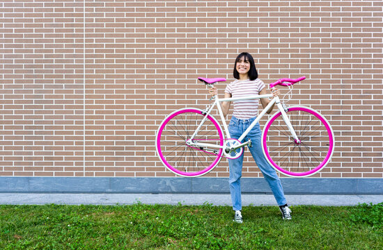 Smiling young woman carrying bicycle in front of wall