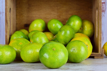 Close up, tangerine with green skin, more units behind in a group, next to a lying wooden box.