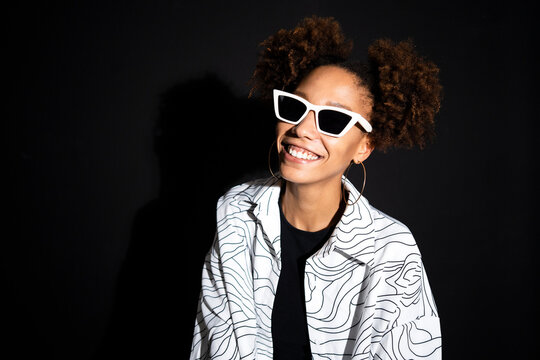 Happy fashionable woman wearing white sunglasses against black background